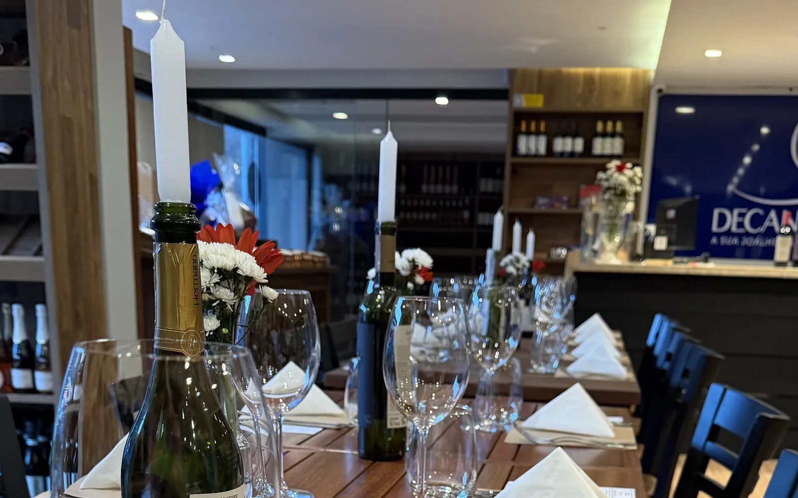 Mesa longa preparada para um evento no salão da Decanter, com velas, flores e taças