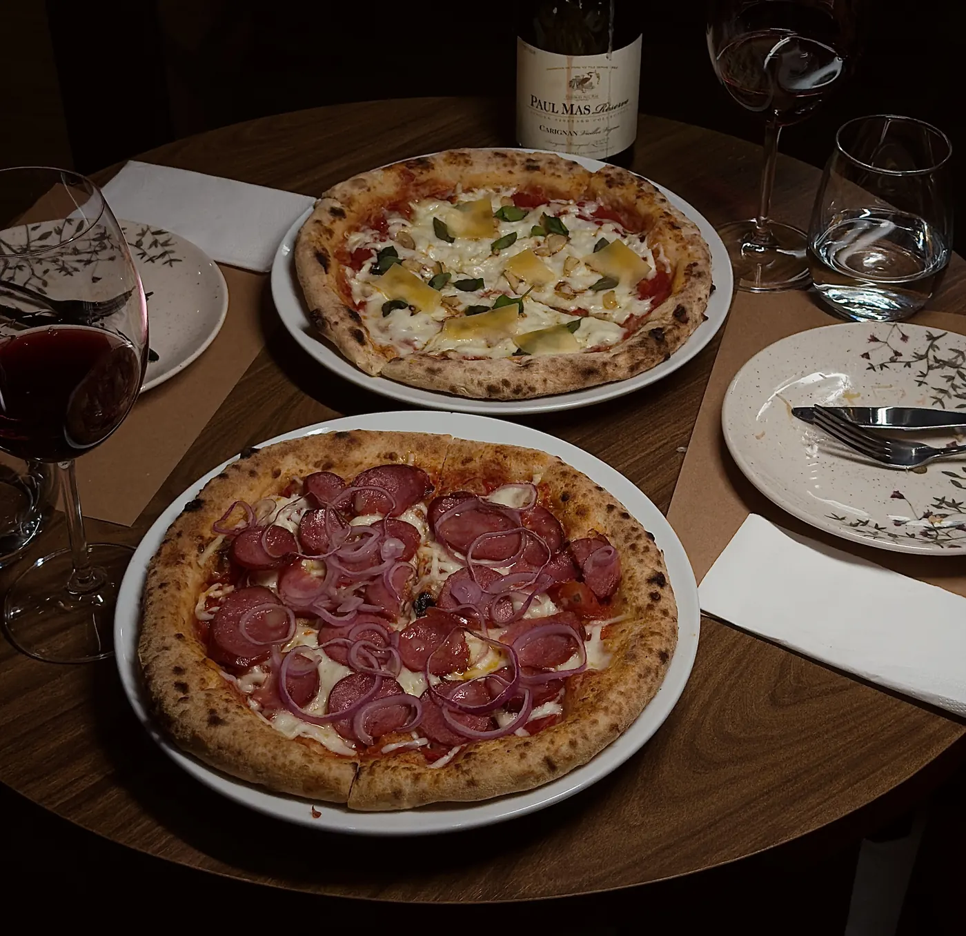 Pizzas, taças de vinho e garrafa Paul Mas em uma mesa da Decanter